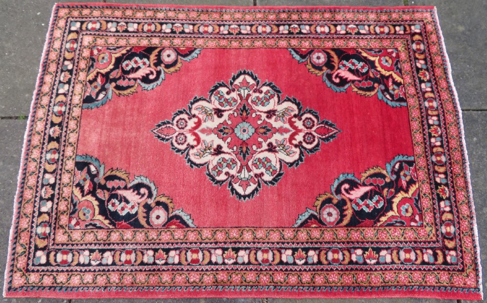 An antique Jozan Persian rug featuring a central floral medallion on a rose red field surrounded by intricate spandrels and multi-band patterned borders. View III