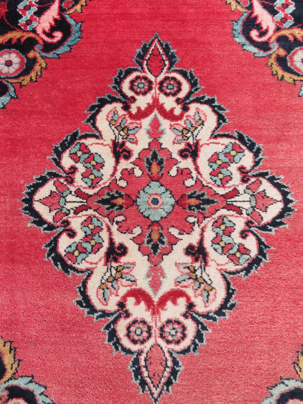 An antique Jozan Persian rug featuring a central floral medallion on a rose red field surrounded by intricate spandrels and multi-band patterned borders. View IV