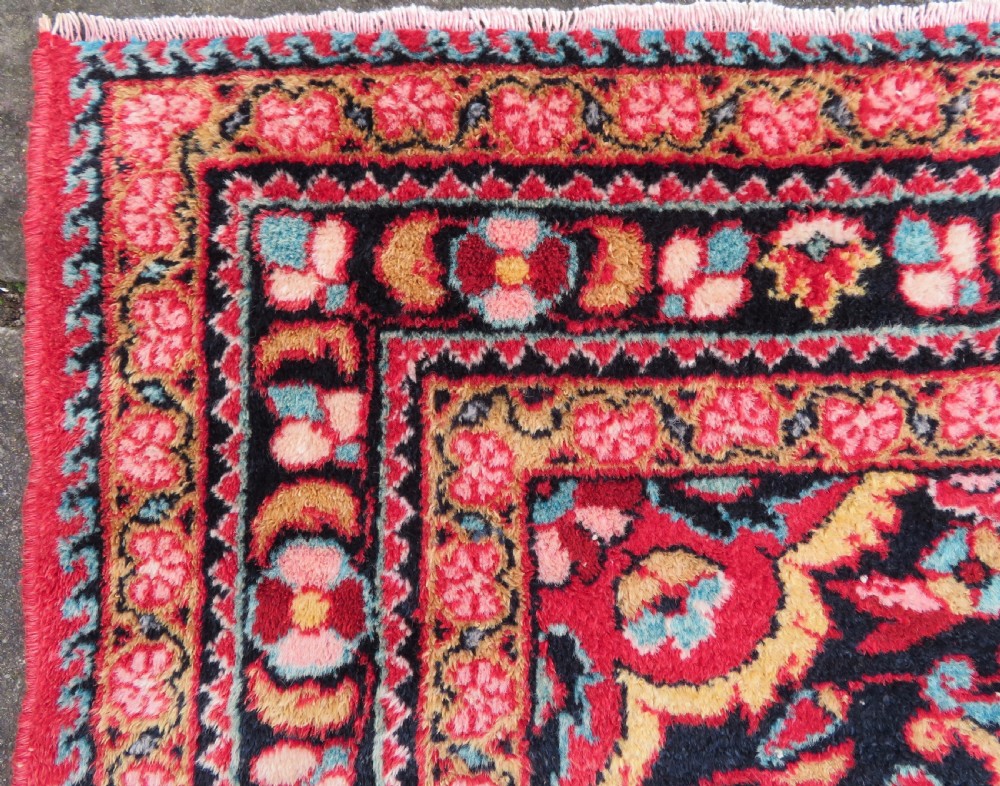 An antique Jozan Persian rug featuring a central floral medallion on a rose red field surrounded by intricate spandrels and multi-band patterned borders. View VI