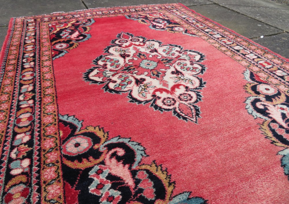 An antique Jozan Persian rug featuring a central floral medallion on a rose red field surrounded by intricate spandrels and multi-band patterned borders. View VIII