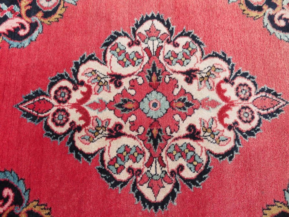 An antique Jozan Persian rug featuring a central floral medallion on a rose red field surrounded by intricate spandrels and multi-band patterned borders. View XII