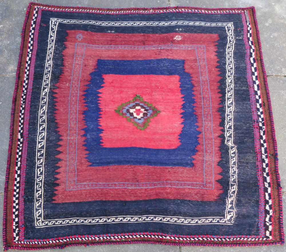 Square flatwoven antique Afshar sofreh rug featuring a central pink diamond medallion framed by nested red and navy blue stepped geometric borders.
