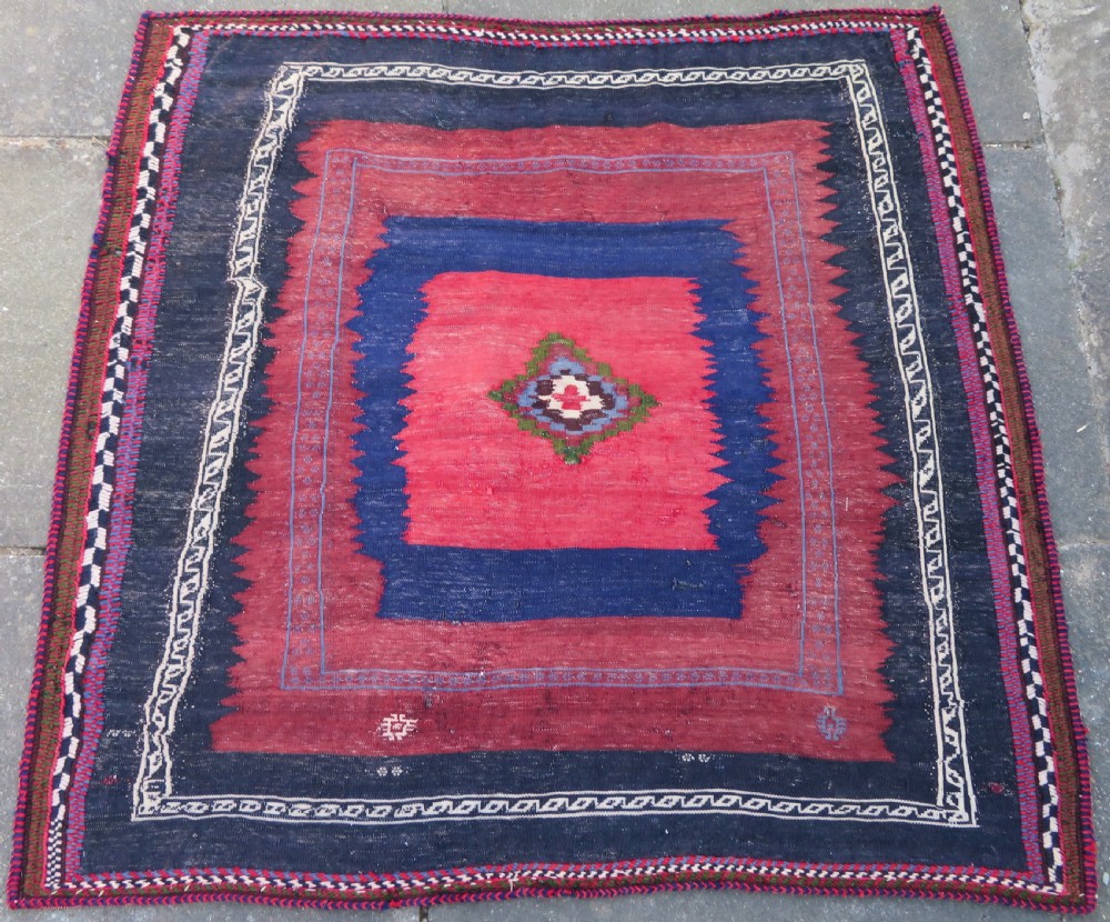 Square flatwoven antique Afshar sofreh rug featuring a central pink diamond medallion framed by nested red and navy blue stepped geometric borders. View II