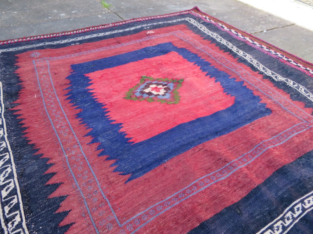Square flatwoven antique Afshar sofreh rug featuring a central pink diamond medallion framed by nested red and navy blue stepped geometric borders. View XVII