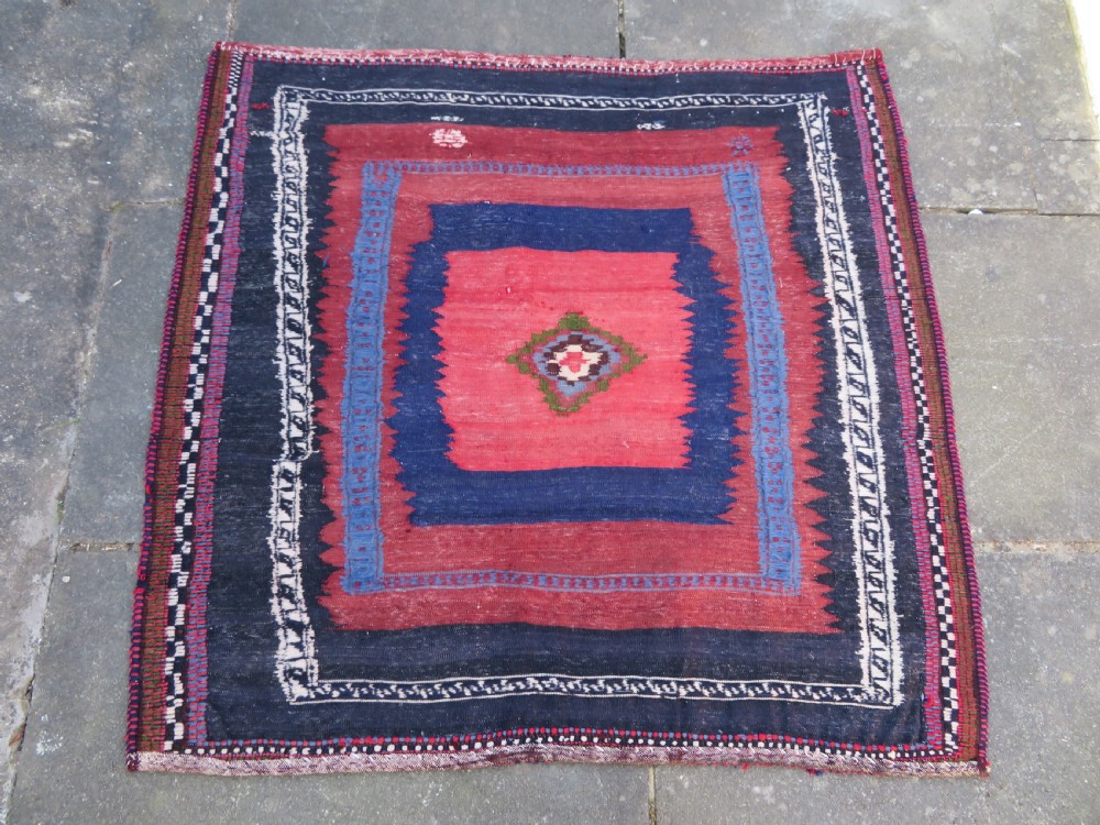 Square flatwoven antique Afshar sofreh rug featuring a central pink diamond medallion framed by nested red and navy blue stepped geometric borders. View XX