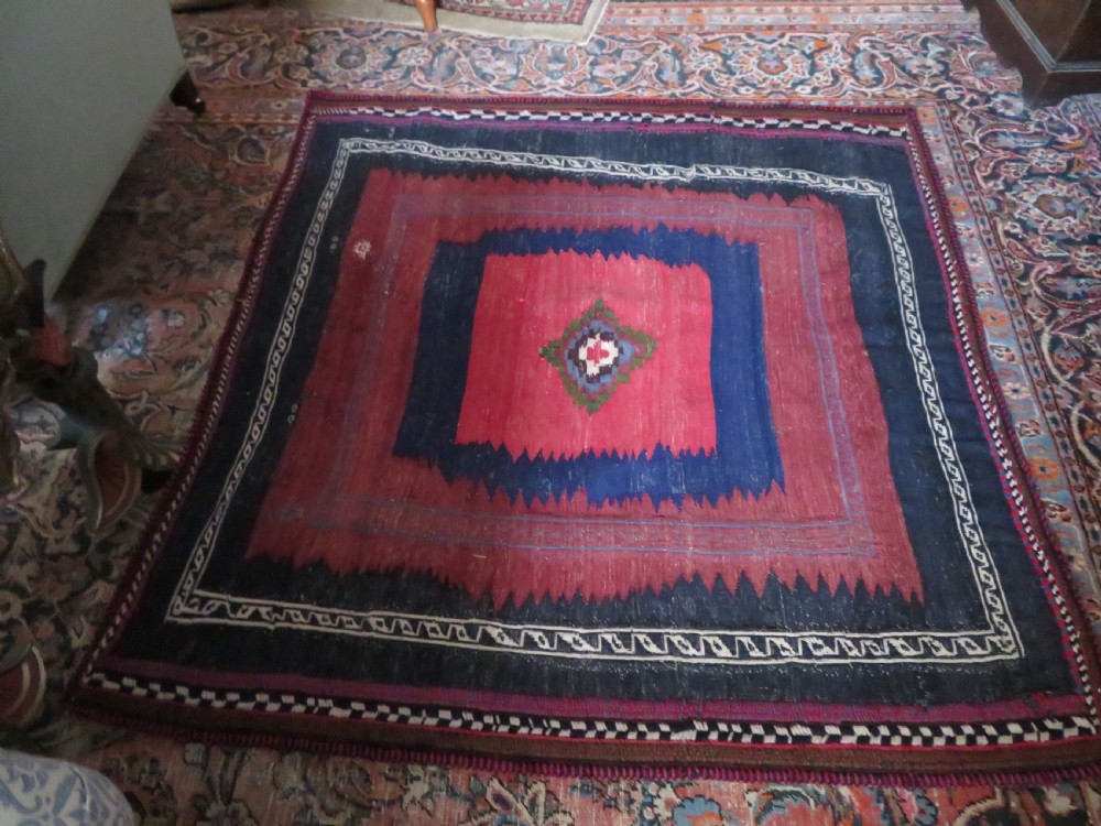 Square flatwoven antique Afshar sofreh rug featuring a central pink diamond medallion framed by nested red and navy blue stepped geometric borders. View XXVIII