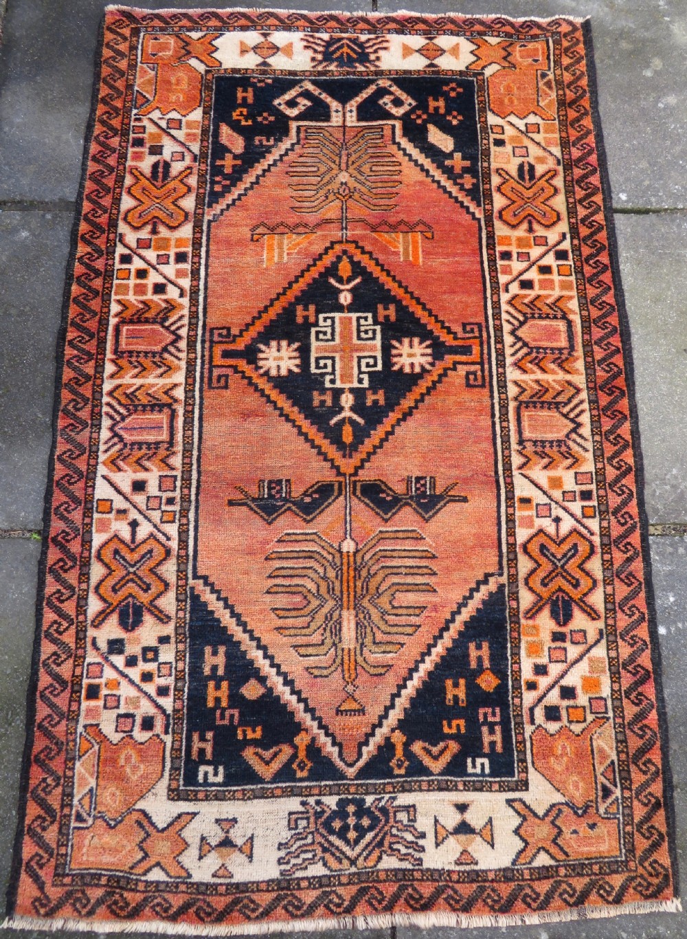 An antique hand-knotted Turkish Kurdish wool rug featuring a central terracotta diamond medallion surrounded by geometric motifs in dark indigo, cream, and orange shades.