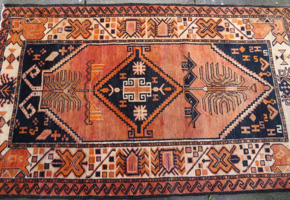 An antique hand-knotted Turkish Kurdish wool rug featuring a central terracotta diamond medallion surrounded by geometric motifs in dark indigo, cream, and orange shades. View III