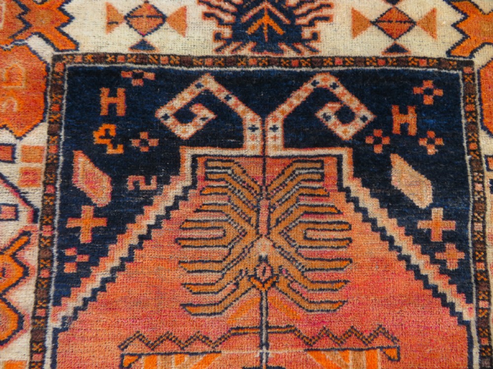 An antique hand-knotted Turkish Kurdish wool rug featuring a central terracotta diamond medallion surrounded by geometric motifs in dark indigo, cream, and orange shades. View IV