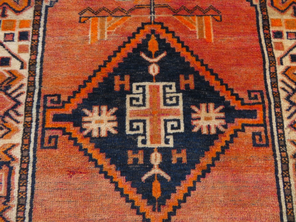 An antique hand-knotted Turkish Kurdish wool rug featuring a central terracotta diamond medallion surrounded by geometric motifs in dark indigo, cream, and orange shades. View V