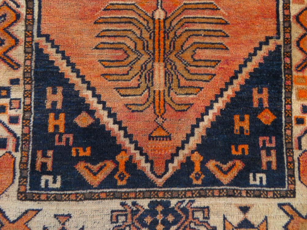 An antique hand-knotted Turkish Kurdish wool rug featuring a central terracotta diamond medallion surrounded by geometric motifs in dark indigo, cream, and orange shades. View VI