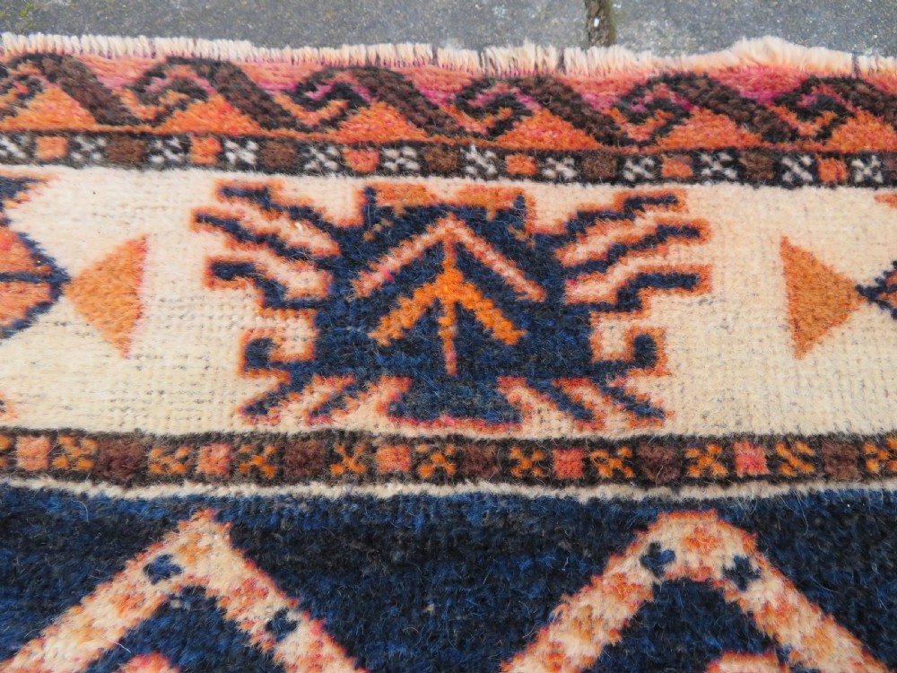 An antique hand-knotted Turkish Kurdish wool rug featuring a central terracotta diamond medallion surrounded by geometric motifs in dark indigo, cream, and orange shades. View XIV