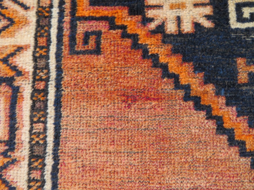 An antique hand-knotted Turkish Kurdish wool rug featuring a central terracotta diamond medallion surrounded by geometric motifs in dark indigo, cream, and orange shades. View XVI