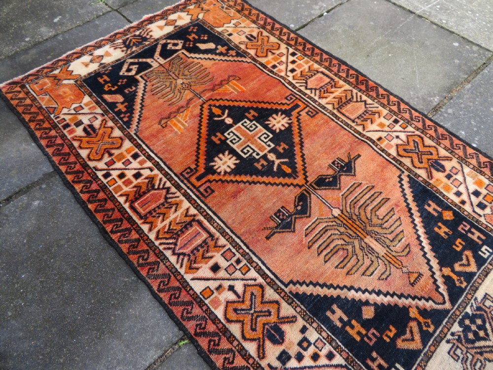 An antique hand-knotted Turkish Kurdish wool rug featuring a central terracotta diamond medallion surrounded by geometric motifs in dark indigo, cream, and orange shades. View XVII