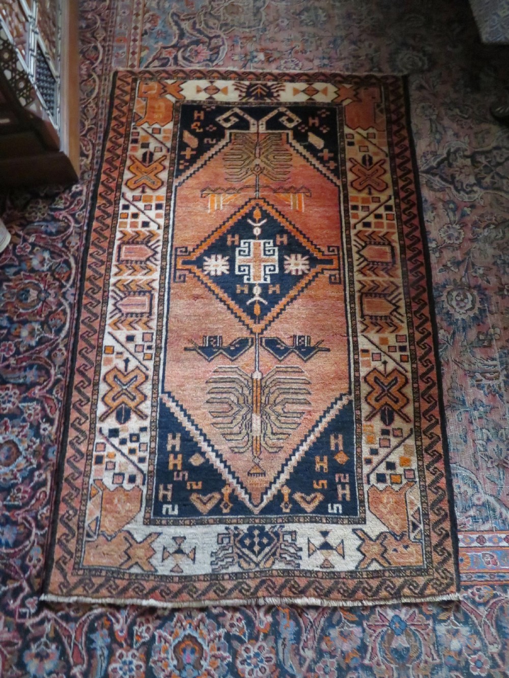 An antique hand-knotted Turkish Kurdish wool rug featuring a central terracotta diamond medallion surrounded by geometric motifs in dark indigo, cream, and orange shades. View XXI
