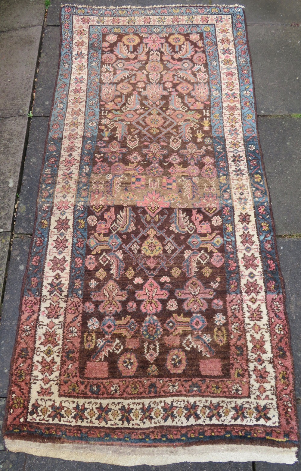 An antique Kurdish wool runner rug featuring a dark brown central field filled with pink and blue geometric motifs surrounded by a cream floral border. View II