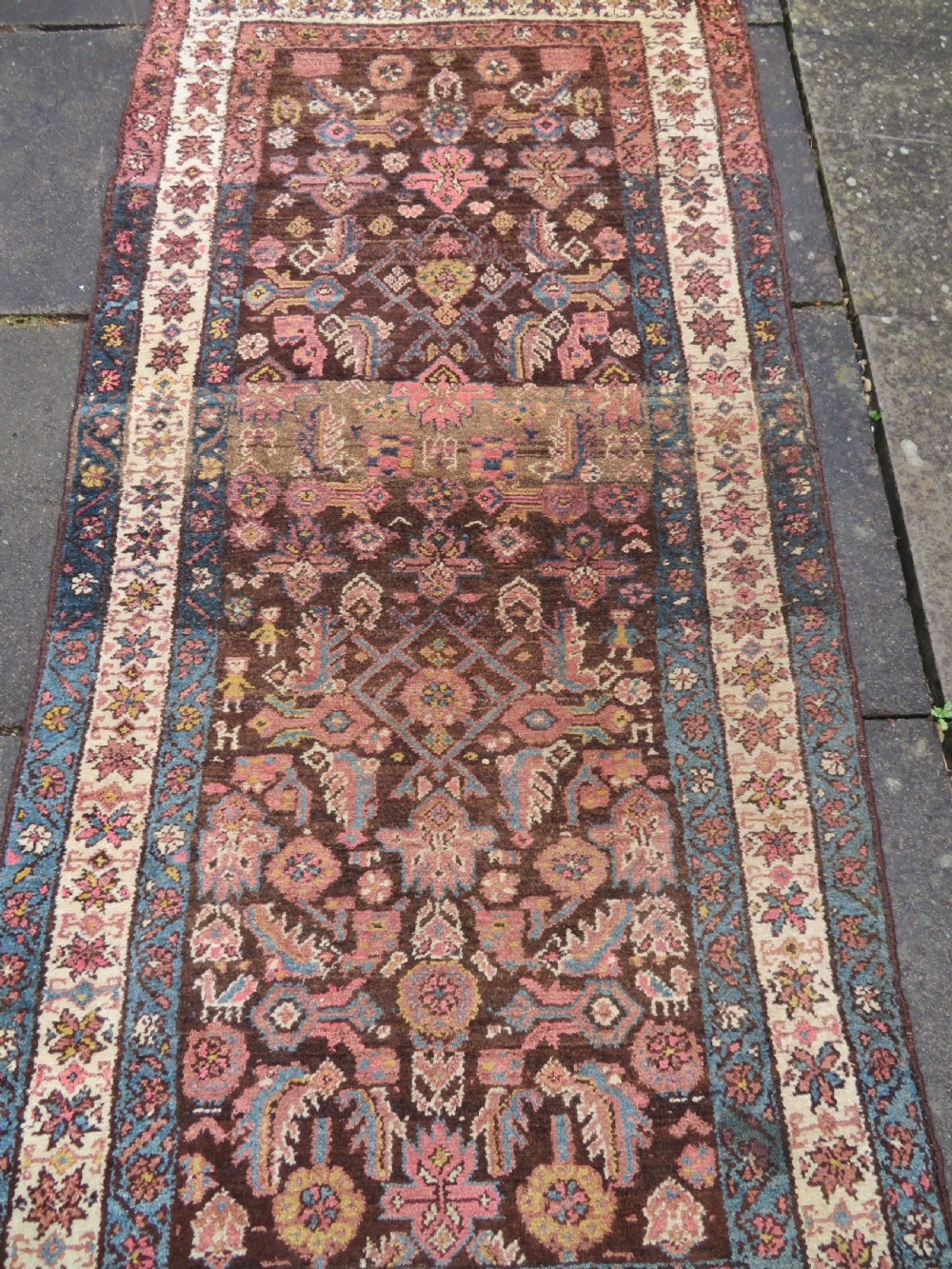 An antique Kurdish wool runner rug featuring a dark brown central field filled with pink and blue geometric motifs surrounded by a cream floral border. View III