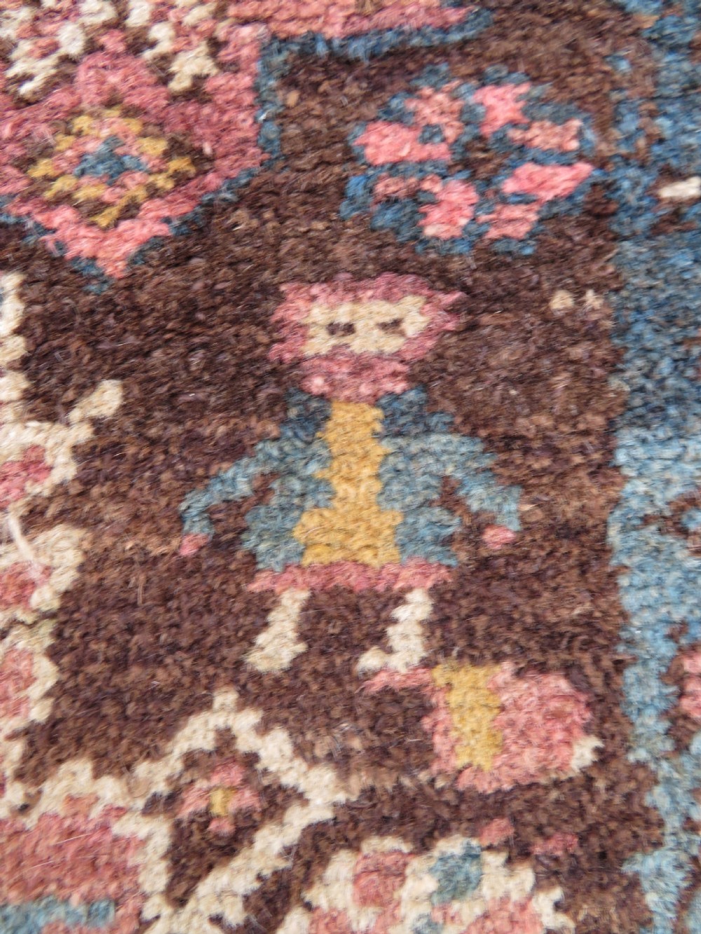 An antique Kurdish wool runner rug featuring a dark brown central field filled with pink and blue geometric motifs surrounded by a cream floral border. View IV