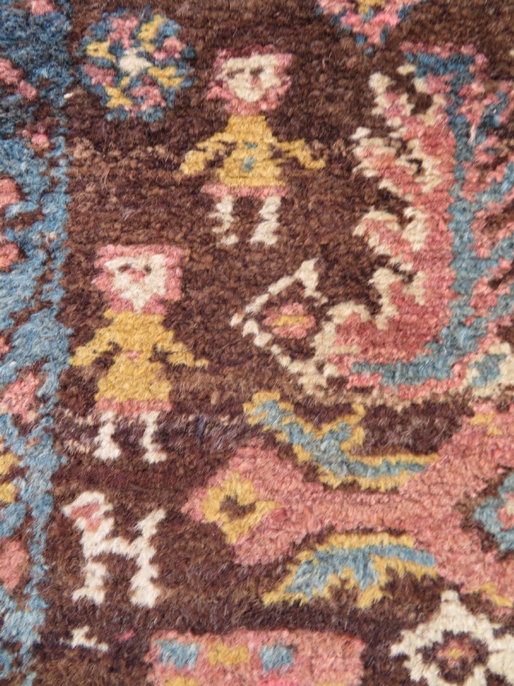An antique Kurdish wool runner rug featuring a dark brown central field filled with pink and blue geometric motifs surrounded by a cream floral border. View V