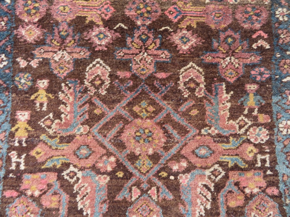 An antique Kurdish wool runner rug featuring a dark brown central field filled with pink and blue geometric motifs surrounded by a cream floral border. View VI