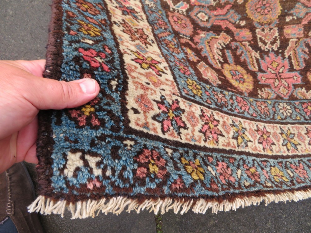An antique Kurdish wool runner rug featuring a dark brown central field filled with pink and blue geometric motifs surrounded by a cream floral border. View IX