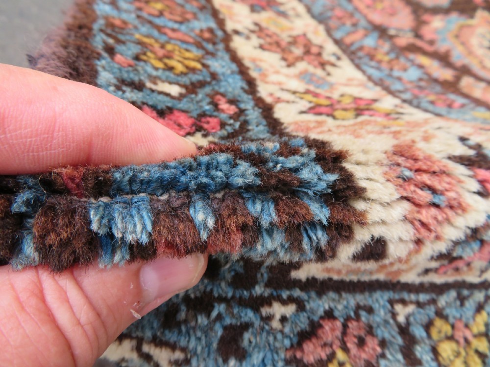 An antique Kurdish wool runner rug featuring a dark brown central field filled with pink and blue geometric motifs surrounded by a cream floral border. View X