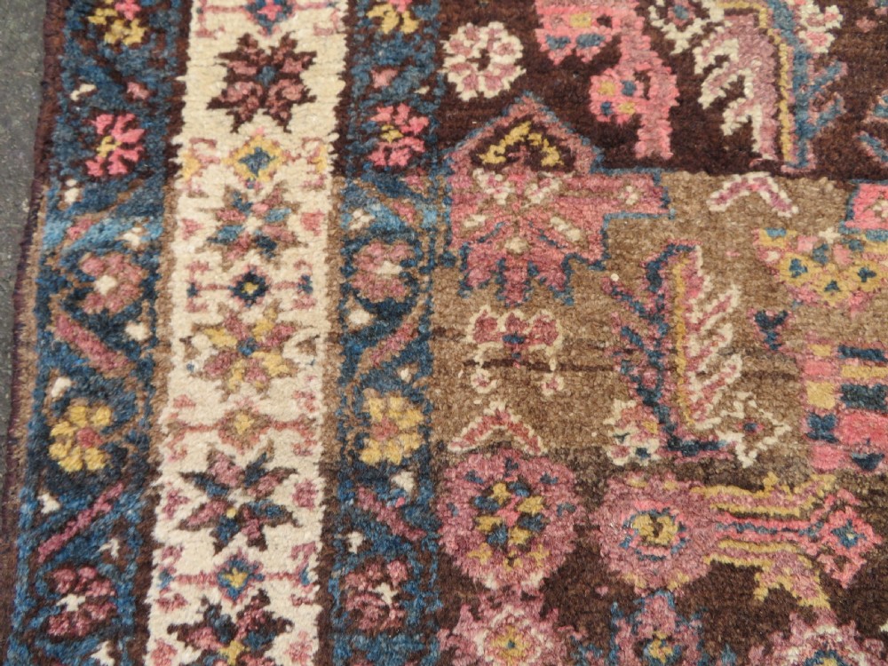 An antique Kurdish wool runner rug featuring a dark brown central field filled with pink and blue geometric motifs surrounded by a cream floral border. View XI