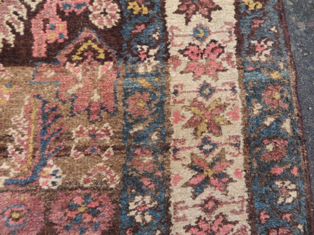An antique Kurdish wool runner rug featuring a dark brown central field filled with pink and blue geometric motifs surrounded by a cream floral border. View XII
