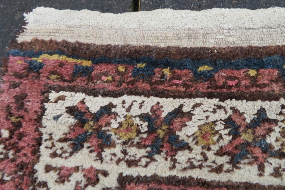 An antique Kurdish wool runner rug featuring a dark brown central field filled with pink and blue geometric motifs surrounded by a cream floral border. View XIII