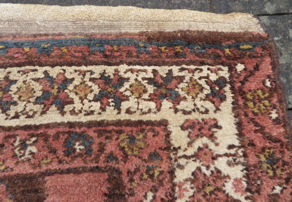 An antique Kurdish wool runner rug featuring a dark brown central field filled with pink and blue geometric motifs surrounded by a cream floral border. View XIV