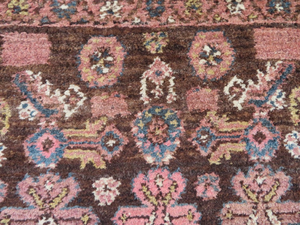 An antique Kurdish wool runner rug featuring a dark brown central field filled with pink and blue geometric motifs surrounded by a cream floral border. View XV