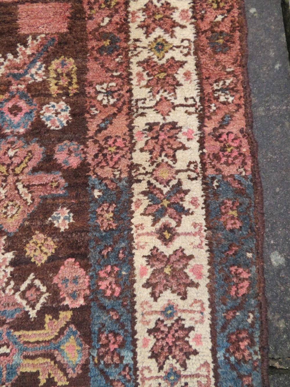An antique Kurdish wool runner rug featuring a dark brown central field filled with pink and blue geometric motifs surrounded by a cream floral border. View XVI