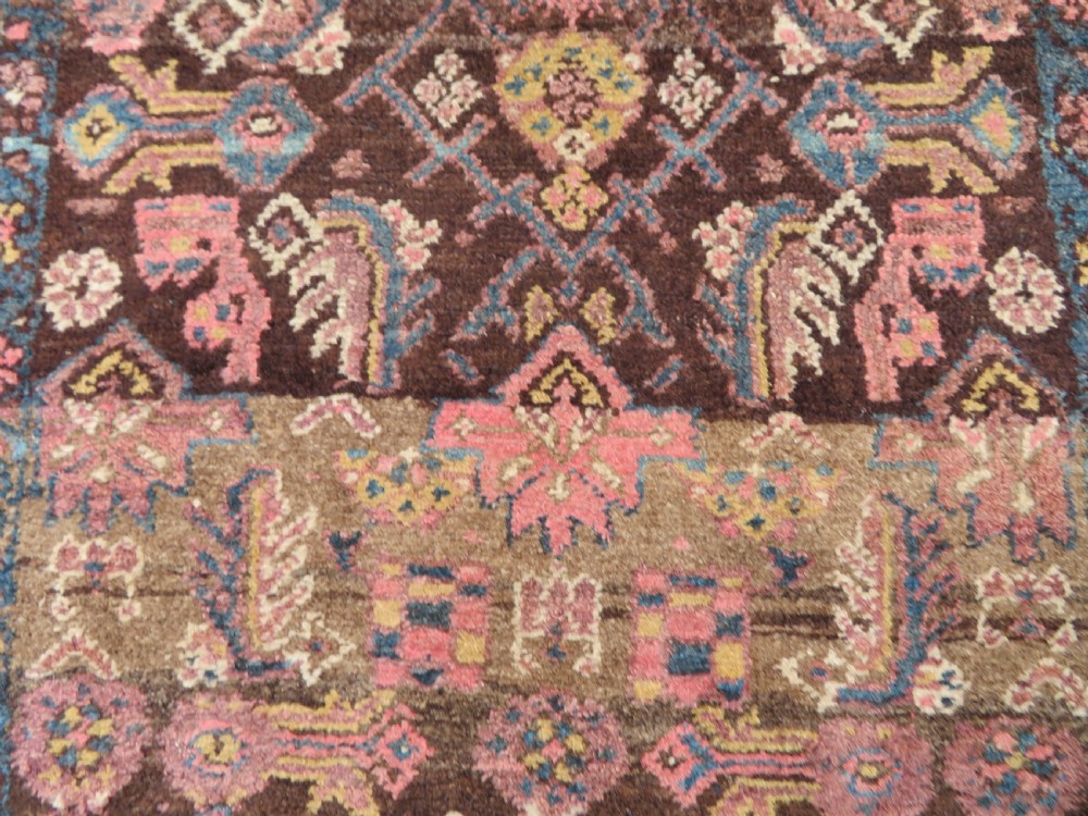 An antique Kurdish wool runner rug featuring a dark brown central field filled with pink and blue geometric motifs surrounded by a cream floral border. View XVII