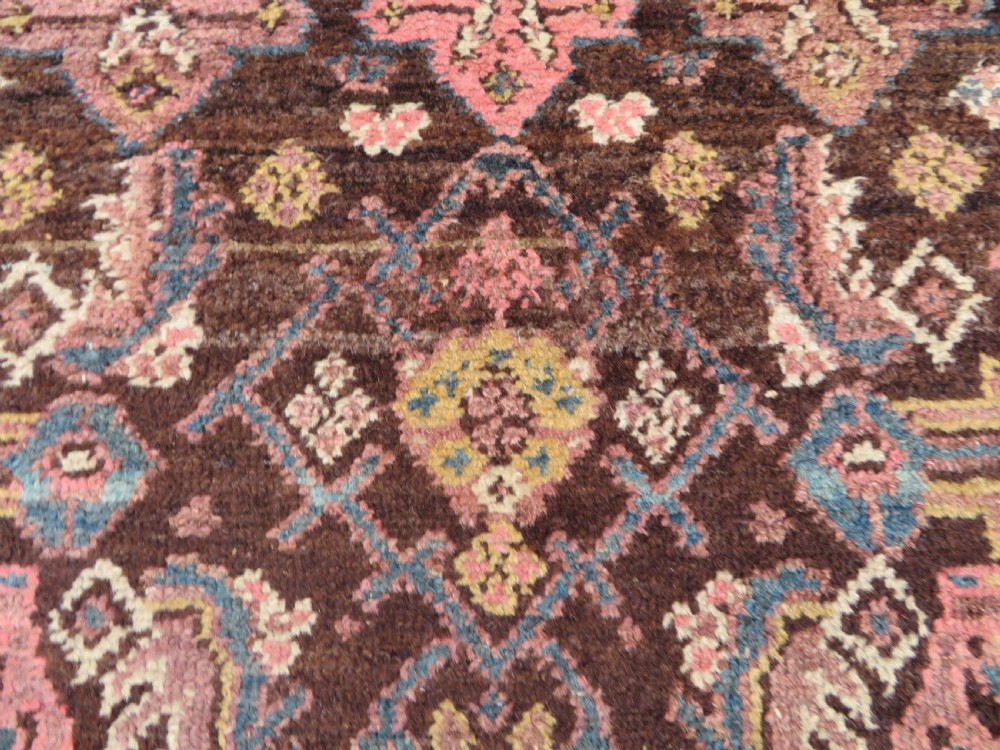 An antique Kurdish wool runner rug featuring a dark brown central field filled with pink and blue geometric motifs surrounded by a cream floral border. View XVIII