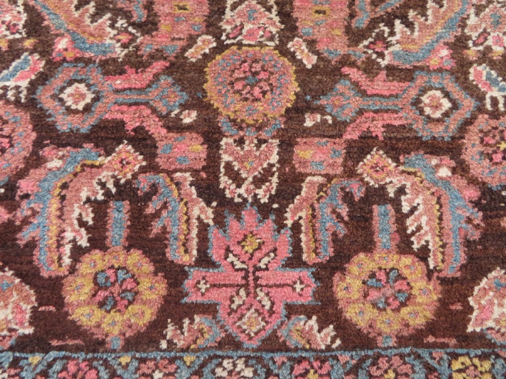 An antique Kurdish wool runner rug featuring a dark brown central field filled with pink and blue geometric motifs surrounded by a cream floral border. View XIX