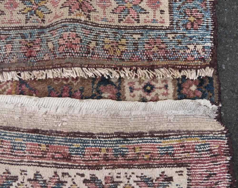 An antique Kurdish wool runner rug featuring a dark brown central field filled with pink and blue geometric motifs surrounded by a cream floral border. View XXII