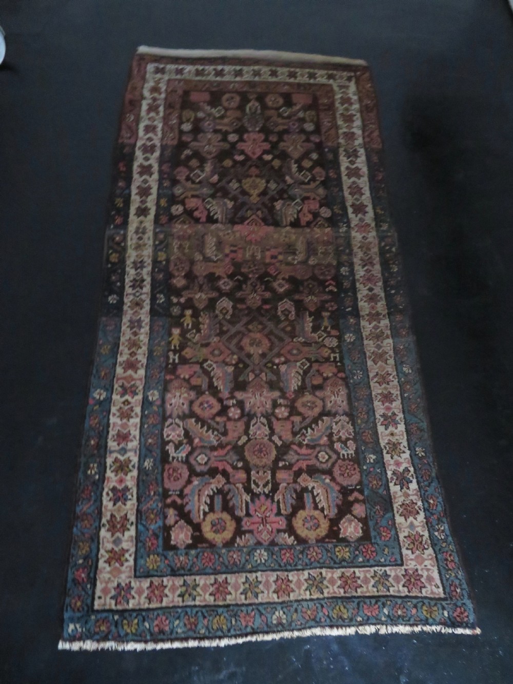 An antique Kurdish wool runner rug featuring a dark brown central field filled with pink and blue geometric motifs surrounded by a cream floral border. View XXIV