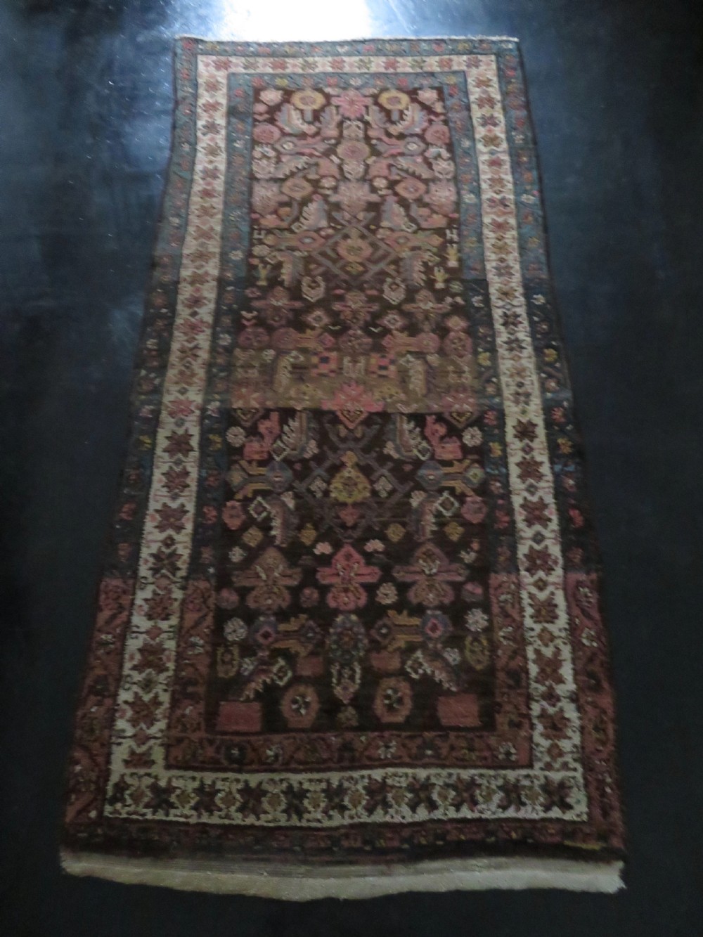 An antique Kurdish wool runner rug featuring a dark brown central field filled with pink and blue geometric motifs surrounded by a cream floral border. View XXV