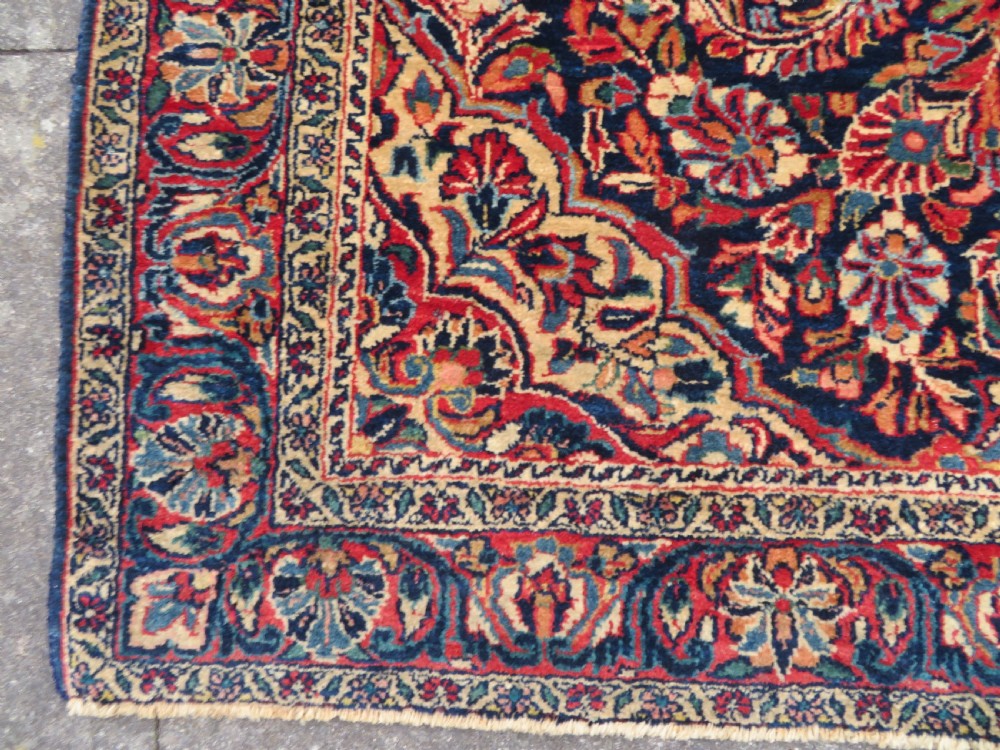 An antique West Persian Sarouk wool rug featuring a detailed central floral medallion framed by dense floral vine scrolls in shades of red, dark navy, cream, and blue. View IX