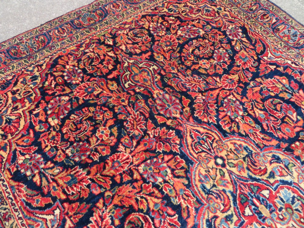 An antique West Persian Sarouk wool rug featuring a detailed central floral medallion framed by dense floral vine scrolls in shades of red, dark navy, cream, and blue. View XV