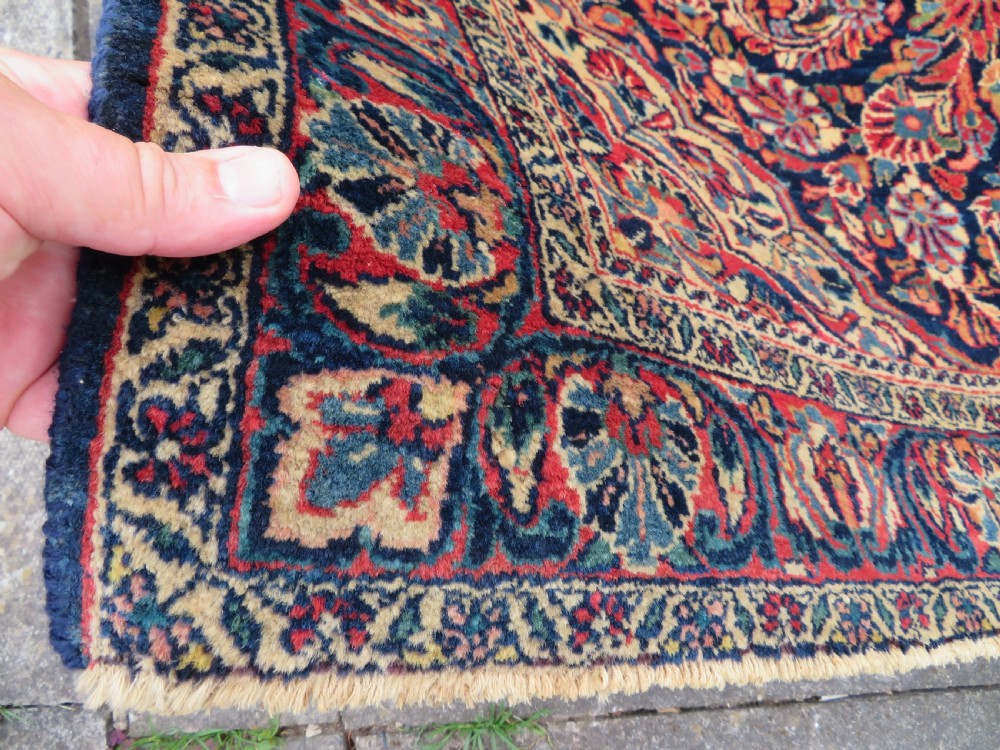 An antique West Persian Sarouk wool rug featuring a detailed central floral medallion framed by dense floral vine scrolls in shades of red, dark navy, cream, and blue. View XVII