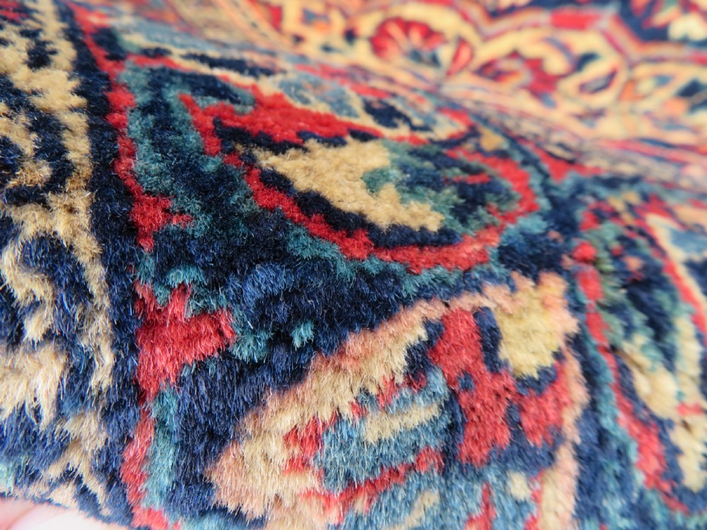 An antique West Persian Sarouk wool rug featuring a detailed central floral medallion framed by dense floral vine scrolls in shades of red, dark navy, cream, and blue. View XVIII