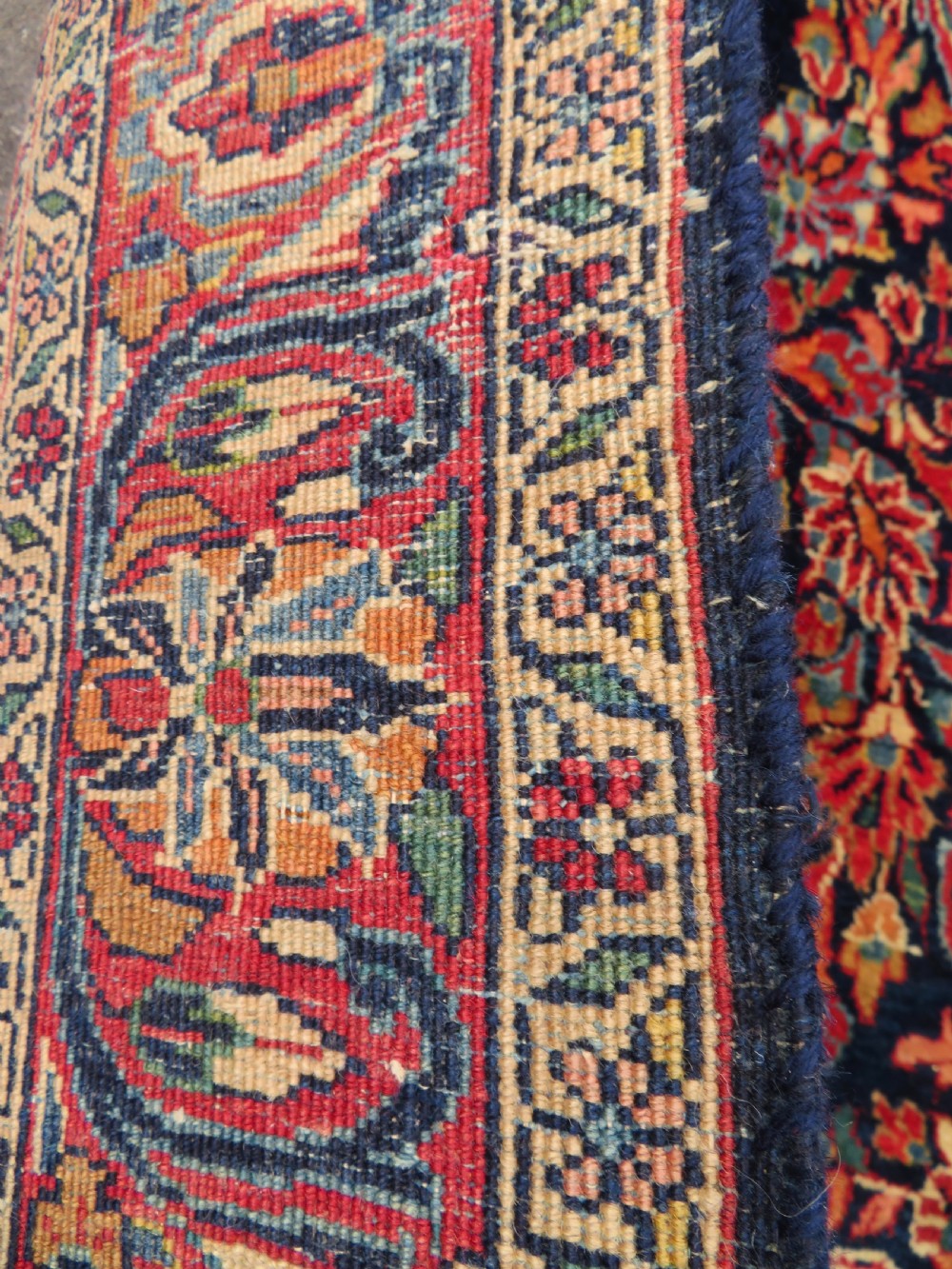 An antique West Persian Sarouk wool rug featuring a detailed central floral medallion framed by dense floral vine scrolls in shades of red, dark navy, cream, and blue. View XX