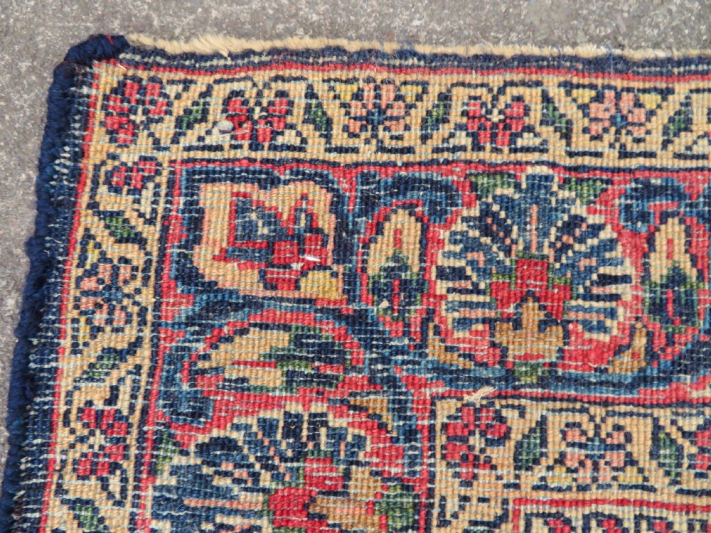 An antique West Persian Sarouk wool rug featuring a detailed central floral medallion framed by dense floral vine scrolls in shades of red, dark navy, cream, and blue. View XXII
