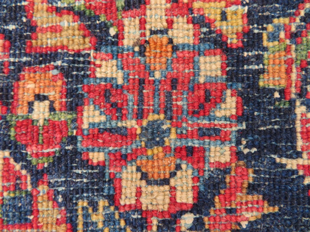 An antique West Persian Sarouk wool rug featuring a detailed central floral medallion framed by dense floral vine scrolls in shades of red, dark navy, cream, and blue. View XXIII