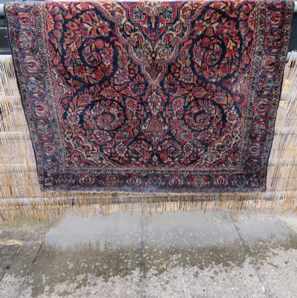 An antique West Persian Sarouk wool rug featuring a detailed central floral medallion framed by dense floral vine scrolls in shades of red, dark navy, cream, and blue. View XXIX