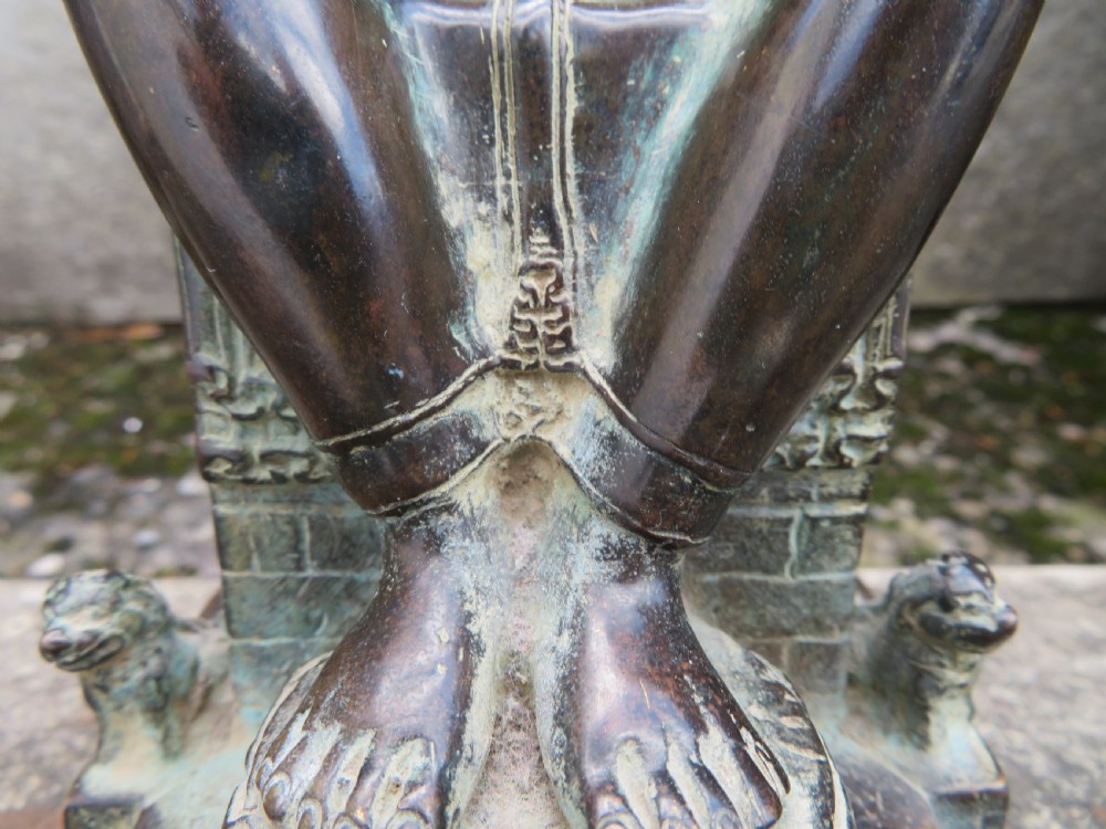 A dark copper alloy sculpture depicting Buddha seated on an ornate throne with legs lowered in the European posture. View VIII