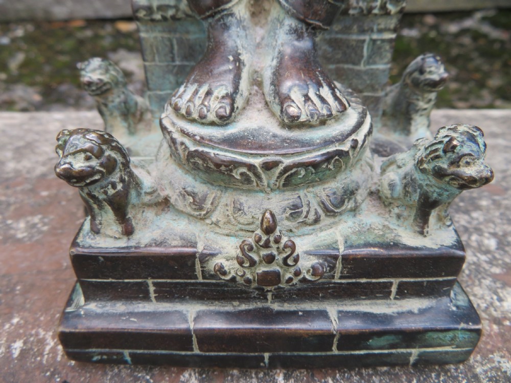 A dark copper alloy sculpture depicting Buddha seated on an ornate throne with legs lowered in the European posture. View IX
