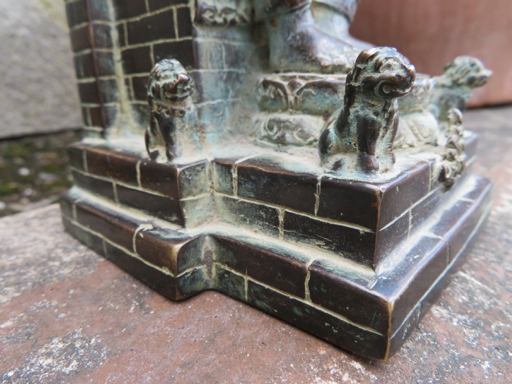 A dark copper alloy sculpture depicting Buddha seated on an ornate throne with legs lowered in the European posture. View X