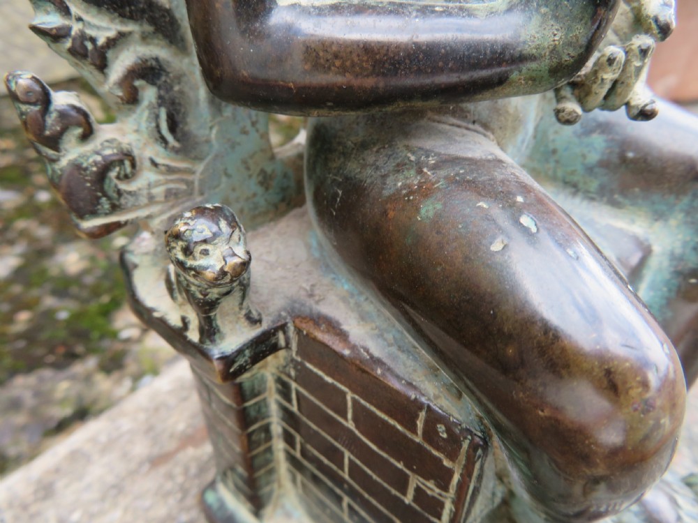 A dark copper alloy sculpture depicting Buddha seated on an ornate throne with legs lowered in the European posture. View XXIX